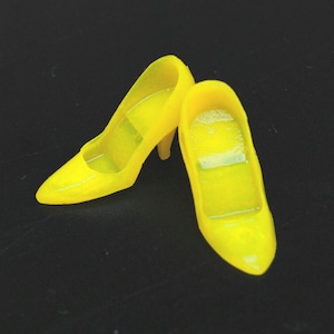 May include: A pair of bright yellow high-heeled shoes. The shoes are made of a shiny plastic material and have a simple, classic design.