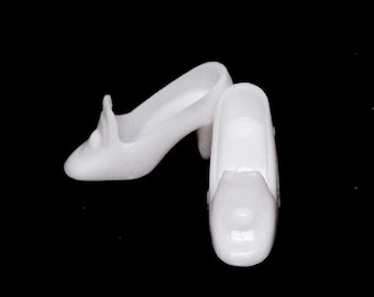 May include: A pair of white high-heeled shoes. The shoes have a classic design with a pointed toe and a small heel. The shoes are made of a smooth, glossy material and are set against a black background.