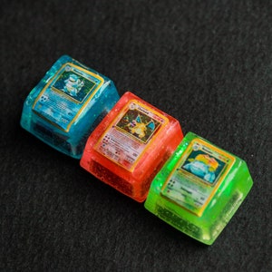 Peut inclure: Trois touches de clavier carrées en résine avec des cartes à collectionner miniatures intégrées. La touche bleue affiche Tortank, la rouge Dracaufeu et la verte Florizarre. Chaque touche translucide présente une finition scintillante.