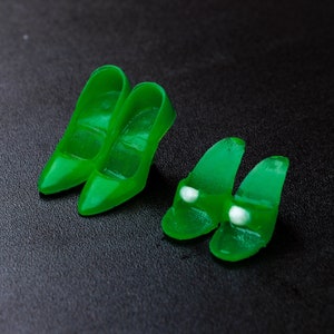May include: Four pairs of green plastic doll shoes. Two pairs are high heels and two pairs are flat sandals.