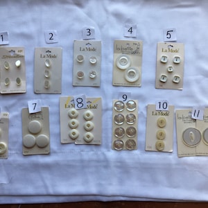May include: Assortment of white plastic buttons on cards. The cards are labeled with numbers 1 through 11. Some cards have the brand name "La Mode" or "La Petite" printed on them.