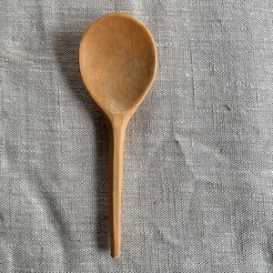 Könnte beinhalten: Ein Holzlöffel mit einem langen, schlanken Stiel. Der Löffel ist aus hellem braunem Holz gefertigt und hat eine glatte, abgerundete Schale.