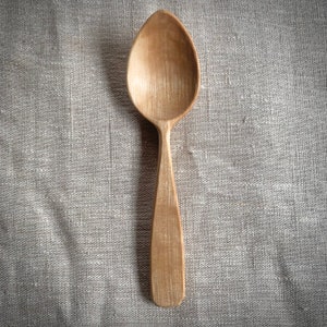 Könnte beinhalten: Ein Holzlöffel mit natürlicher Oberfläche. Der Löffel ist aus hellbraunem Holz gefertigt und hat eine abgerundete Schale und einen langen Stiel.