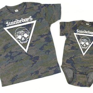 May include: Two matching camouflage print shirts. One is a short-sleeved t-shirt, and the other is a baby onesie. Both have a white triangle with a skull graphic and the text "$uicideboy$".