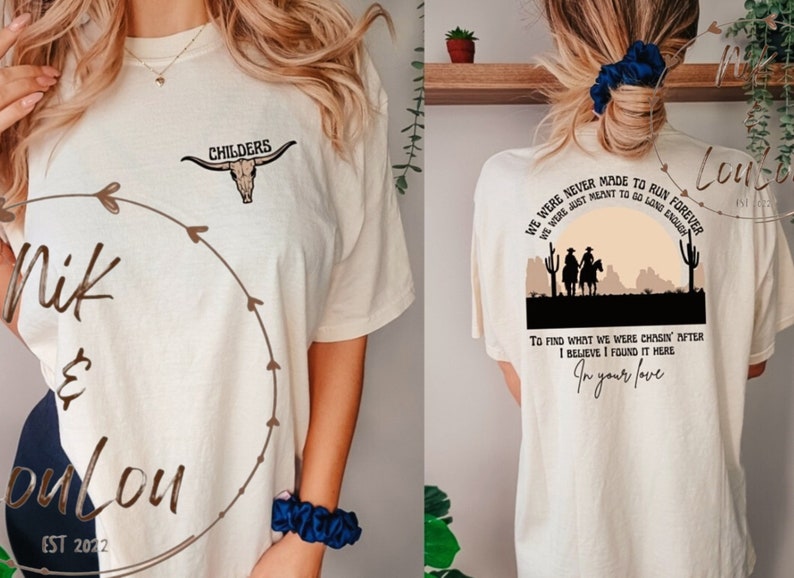 K&ouml;nnte beinhalten: Ein beiges T-Shirt mit einem braunen Sch&auml;del und dem Text "CHILDERS" auf der Vorderseite. Die R&uuml;ckseite des Shirts zeigt eine Sonnenuntergangsszene mit zwei Cowboys auf Pferden und dem Text "WE WERE NEVER MADE TO RUN FOREVER WE WERE JUST MEANT TO GO LONG ENOUGH TO FIND WHAT WE WERE CHASIN' AFTER I BELIEVE I FOUND IT HERE In your love".