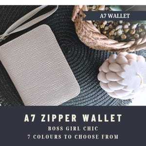 May include: A light beige A7 zipper wallet with a textured finish and a wrist strap. The wallet is rectangular and rests on a dark, textured surface. The image also features a small basket and a decorative item. Text on the image reads "A7 Wallet" and "A7 Zipper Wallet".