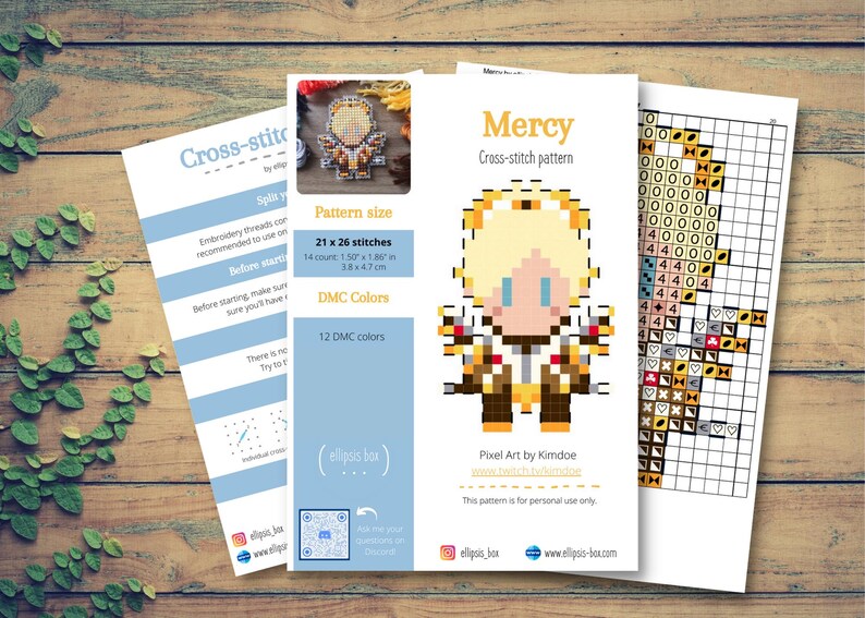 May include: Cross-stitch pattern featuring a pixel art design of a character named Mercy. The pattern size is 1.50 x 1.86 inches, with 21 x 26 stitches. The design uses 12 DMC colors. The image is on a wooden surface.