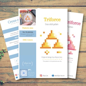 May include: Three white cross-stitch pattern sheets with the text "Triforce" and a pixelated triangle design. The pattern size is 16 x 16 stitches, 2.9 x 2.9 cm. The sheets are on a wooden surface.