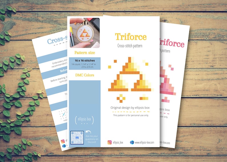 May include: Three white cross-stitch pattern sheets with the text "Triforce" and a pixelated triangle design. The pattern size is 16 x 16 stitches, 2.9 x 2.9 cm. The sheets are on a wooden surface.