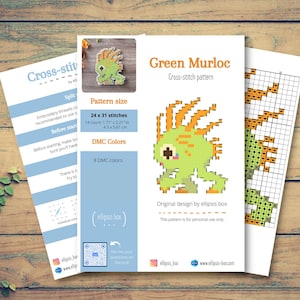 May include: Three sheets of paper on a wooden surface. The central sheet features a green pixelated Murloc cross-stitch pattern with orange accents. The pattern size is 1.71 x 2.21 inches (4.3 x 5.61 cm). The text reads "Green Murloc Cross-stitch pattern".
