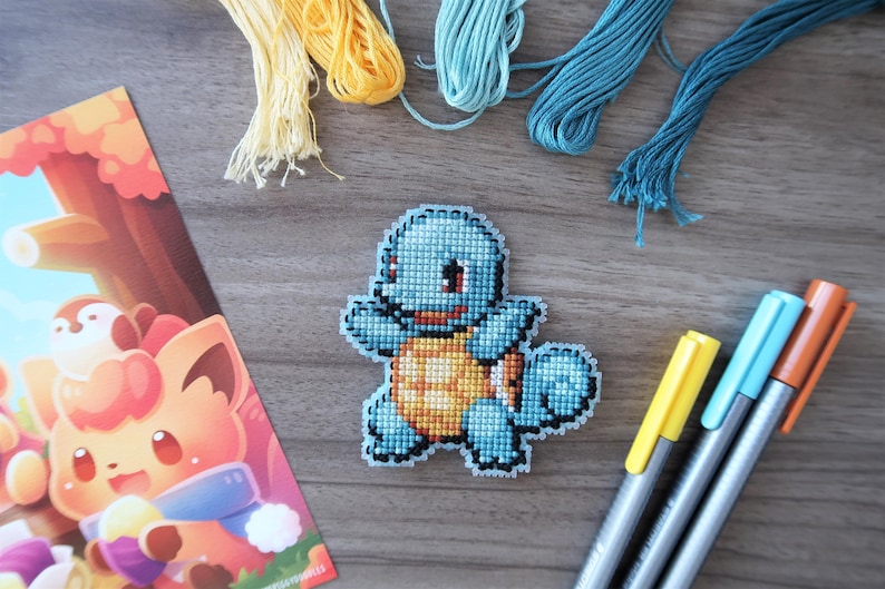 May include: A handmade cross-stitch of a blue cartoon turtle with a yellow belly, surrounded by embroidery floss and colorful markers. A colorful illustration of a fox is also present.