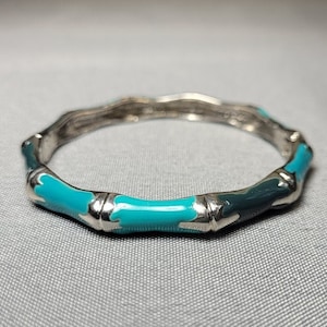 May include: A silver bangle bracelet with a turquoise and black enamel design. The bracelet is made to look like a series of connected bamboo stalks.