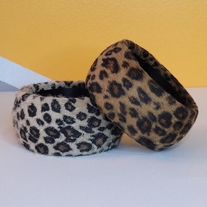 May include: Two leopard print fabric headbands. One is brown and black, the other is white, brown, and black.