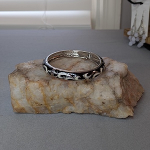 Svart med vitt vinmönster, emaljmålad, armband i legeringsmetall med gångjärn. Välj silver- eller guldfärgad insida.