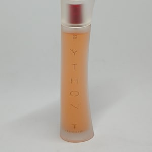 Peut inclure: Un flacon de parfum Trussardi Python en verre transparent avec un bouchon rouge. Le flacon a la forme d'un rectangle incurvé et porte le mot "Python" imprimé verticalement sur le devant en lettres dorées.