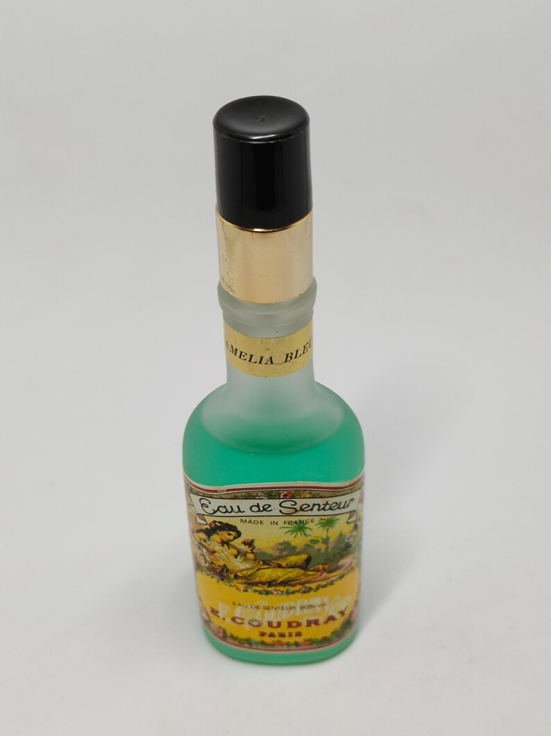 Puede incluir: Un frasco de perfume vintage con tapa negra y banda dorada. El frasco contiene l&iacute;quido verde y tiene una etiqueta con el texto "Eau de Senteur" y una ilustraci&oacute;n de mujer. El frasco est&aacute; etiquetado como "Made in France" y "R. Coudray Paris".