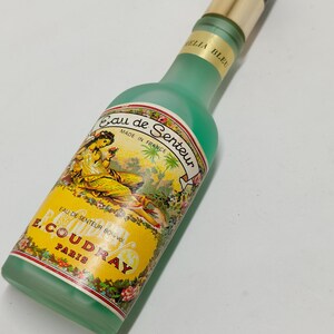 Puede incluir: Un frasco de perfume vintage con un cuerpo de vidrio esmerilado verde y una tapa negra y dorada. La etiqueta presenta el texto "Eau de Senteur" y "E. Coudray Paris". La botella est&aacute; hecha en Francia.