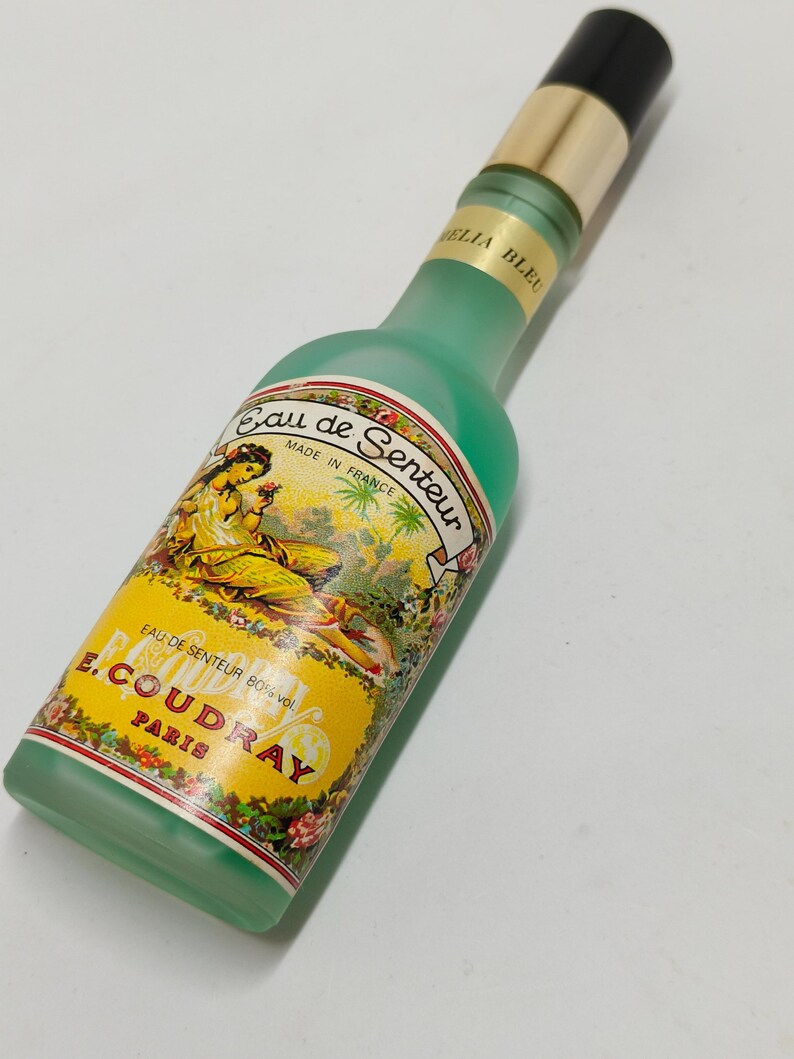 Puede incluir: Un frasco de perfume vintage con un cuerpo de vidrio esmerilado verde y una tapa negra y dorada. La etiqueta presenta el texto "Eau de Senteur" y "E. Coudray Paris". La botella est&aacute; hecha en Francia.