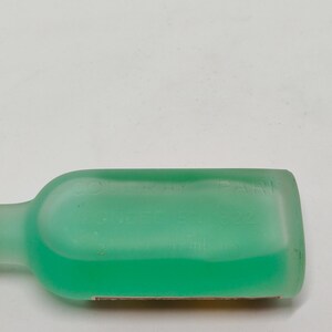 Puede incluir: Una botella transl&uacute;cida de color verde claro con un cuerpo rectangular redondeado y un cuello largo y delgado. La botella contiene un l&iacute;quido verde brillante. El texto "COLORAY PARIS" y "NEE 8.22" es visible en la botella.