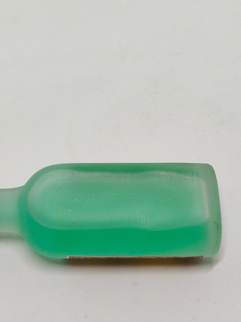 Puede incluir: Una botella transl&uacute;cida de color verde claro con un cuerpo rectangular redondeado y un cuello largo y delgado. La botella contiene un l&iacute;quido verde brillante. El texto "COLORAY PARIS" y "NEE 8.22" es visible en la botella.