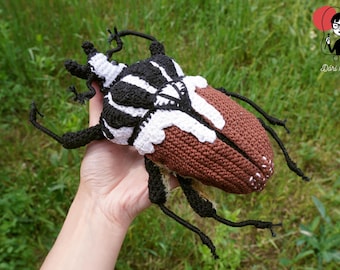 May include: A large, handcrafted crochet beetle featuring a black and white striped thorax and head, with brown wing covers that have white accents at the tips. The insect has six black, jointed legs and detailed, textured yarn stitching.