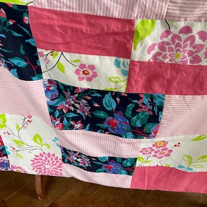 May include: A patchwork quilt featuring a range of floral patterns in pink, blue, green, and white. The quilt is crafted from various fabrics and textures, resulting in a distinctive and appealing design.