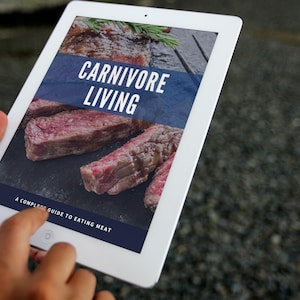 May include: A white tablet computer displaying a digital book cover with the title "Carnivore Living: A Complete Guide to Eating Meat". The cover features a close-up of raw meat.