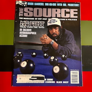 May include: The Source magazine cover featuring rapper MC Eiht. The cover features a photo of MC Eiht wearing a black jacket, a black baseball cap with the word "Compton" on it, and a gold watch. The cover text reads "MC Eiht: Tales from the Hood. An Exclusive Autobiographical Account."