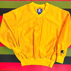 May include: A bright yellow Starter brand pullover windbreaker with a V-neck collar, elastic cuffs, and a ribbed hem. The Starter logo is visible on the chest and sleeve. The windbreaker is made of a lightweight, shiny material.