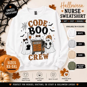 May include: A white crewneck sweatshirt featuring a graphic of three ghosts dressed as medical staff with a crash cart and the text CODE BOO CREW. The design includes a spiderweb, bats, and orange accents. The sweatshirt is shown with color options.