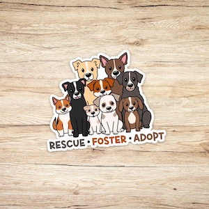 May include: A sticker featuring a group of cartoon dogs in various colors, including brown, black, and white. The dogs are arranged in a cluster, with the words "RESCUE • FOSTER • ADOPT" in brown text at the bottom. The background is a light brown wood grain.