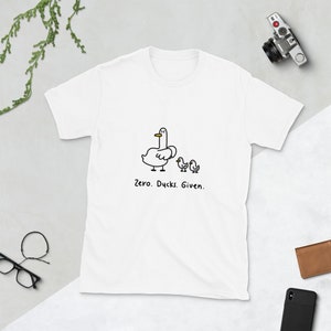 May include: White t-shirt with a black and white illustration of three ducks. The text "Zero. Ducks. Given." is printed below the ducks.
