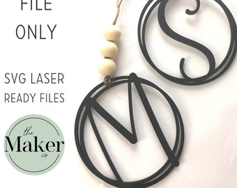 May include: Two black metal circles with the letters "M" and "S" cut out, hanging from a string with wooden beads. The text "DIGITAL FILE ONLY" and "SVG LASER READY FILES" is printed on a white background. The text "the Maker co." is printed in a circle with a green background.