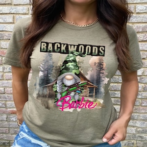 May include: A green t-shirt with a camouflage gnome holding a gun and the text "Backwoods Barbie" printed on it.