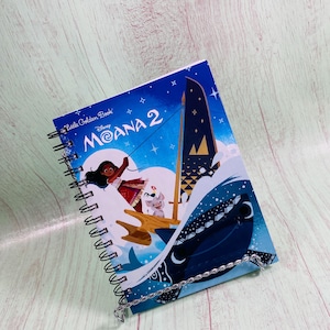 May include: A Little Golden Book featuring Disney's Moana 2. The cover shows Moana sailing on a boat with a blue and white sail, a blue whale, and stars in the background.