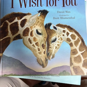 May include: A children's book titled "I Wish for You" with a watercolor illustration of two giraffes. The cover features the title in brown script against a blue sky background. The author and illustrator's names are also visible.