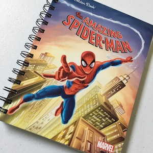 Può includere: Un libro della collezione Little Golden Book con protagonista l'incredibile Spider-Man. La copertina mostra Spider-Man che si dondola attraverso uno skyline cittadino con uno sfondo di tramonto. Il libro ha una rilegatura a spirale nera e il logo Marvel è nell'angolo in basso a destra.