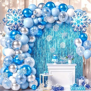 May include: A blue and silver balloon arch with snowflake decorations. The arch is decorated with blue, silver, and white balloons. There are also snowflake-shaped balloons and a blue and white cake on a table in front of the arch.