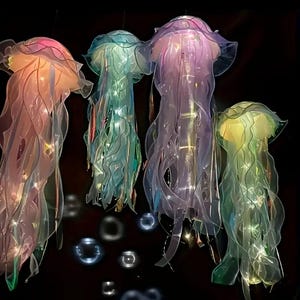 May include: Four hanging jellyfish decorations in shades of pink, blue, purple, and green. The jellyfish have translucent, flowing tentacles and are illuminated with internal lights. The background is black, highlighting the vibrant colors of the jellyfish.