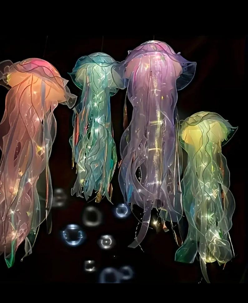 May include: Four hanging jellyfish decorations in shades of pink, blue, purple, and green. The jellyfish have translucent, flowing tentacles and are illuminated with internal lights. The background is black, highlighting the vibrant colors of the jellyfish.