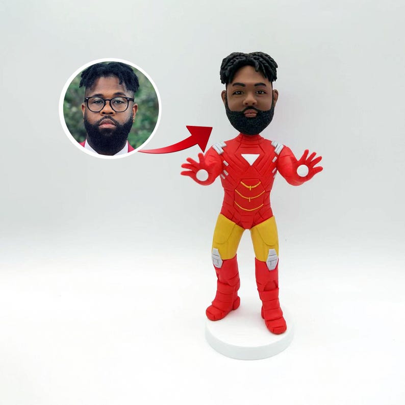 May include: A custom bobblehead figurine of a person wearing a red and yellow Iron Man suit. The person has a black beard and short black hair. The bobblehead is on a white base.