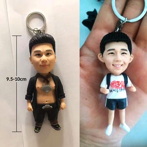 May include: Two 3D printed keychain figurines of people. The figurine on the left is wearing a black jacket, a silver chain, and black pants. The figurine on the right is wearing a white shirt with red text, black shorts, and a white backpack. Both figurines are approximately 9.5-10 cm tall.