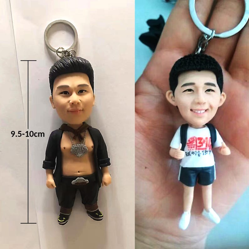 May include: Two 3D printed keychain figurines of people. The figurine on the left is wearing a black jacket, a silver chain, and black pants. The figurine on the right is wearing a white shirt with red text, black shorts, and a white backpack. Both figurines are approximately 9.5-10 cm tall.