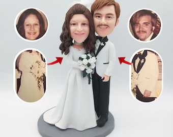 May include: A custom wedding cake topper featuring a bride and groom in a stylized caricature style. The bride is wearing a white wedding dress and holding a bouquet of white flowers. The groom is wearing a black tuxedo with a white bow tie. The couple is standing on a gray base.