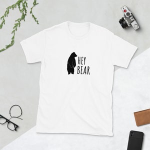 May include: White t-shirt with a black silhouette of a bear and the text "HEY BEAR" printed on the front.