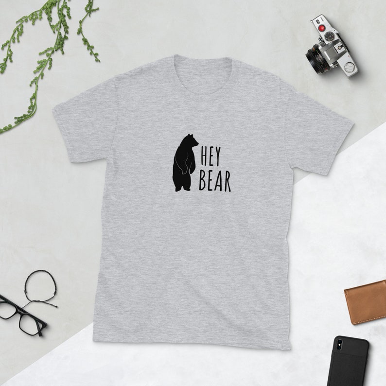 May include: A heather grey t-shirt with a black silhouette of a bear and the text "HEY BEAR" printed on the front.