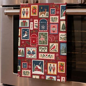 May include: A red kitchen towel featuring a repeating pattern of rectangular postage stamp illustrations. The designs include nutcrackers, reindeer, ice skates, ballet dancers, mailboxes labeled MAIL, North Pole postmarks, and winter foliage.