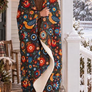 May include: A dark-colored throw blanket featuring a vibrant folk-art pattern of stylized yellow birds and multi-colored flowers in shades of red, orange, blue, and white. The blanket has a thick, cream-colored sherpa fleece lining on the interior.