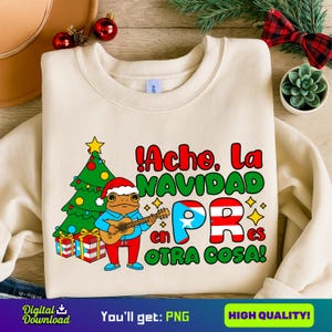 May include: Cream-colored sweatshirt with a festive design. It features a cartoon frog playing a guitar, a Christmas tree, and the text "!Acho, La Navidad en PR es Otra Cosa!" in red, green, and white. The design includes the Puerto Rican flag.