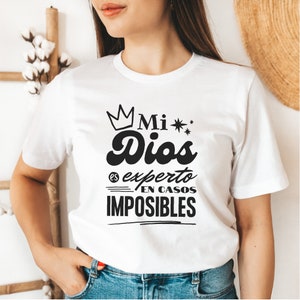 May include: White t-shirt with black text that reads "Mi Dios es experto en casos imposibles" with a crown above the word "Mi".